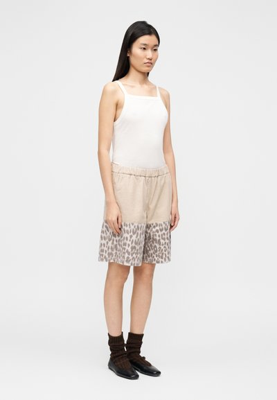 Λευκό αμάνικο μπλουζάκι, συνδυασμένο με μπεζ σορτς που έχουν σχέδιο λεοπάρ στο κάτω μέρος. Το μοντέλο φοράει καφέ ριμπ καλτσάκια και μαύρα παπούτσια.