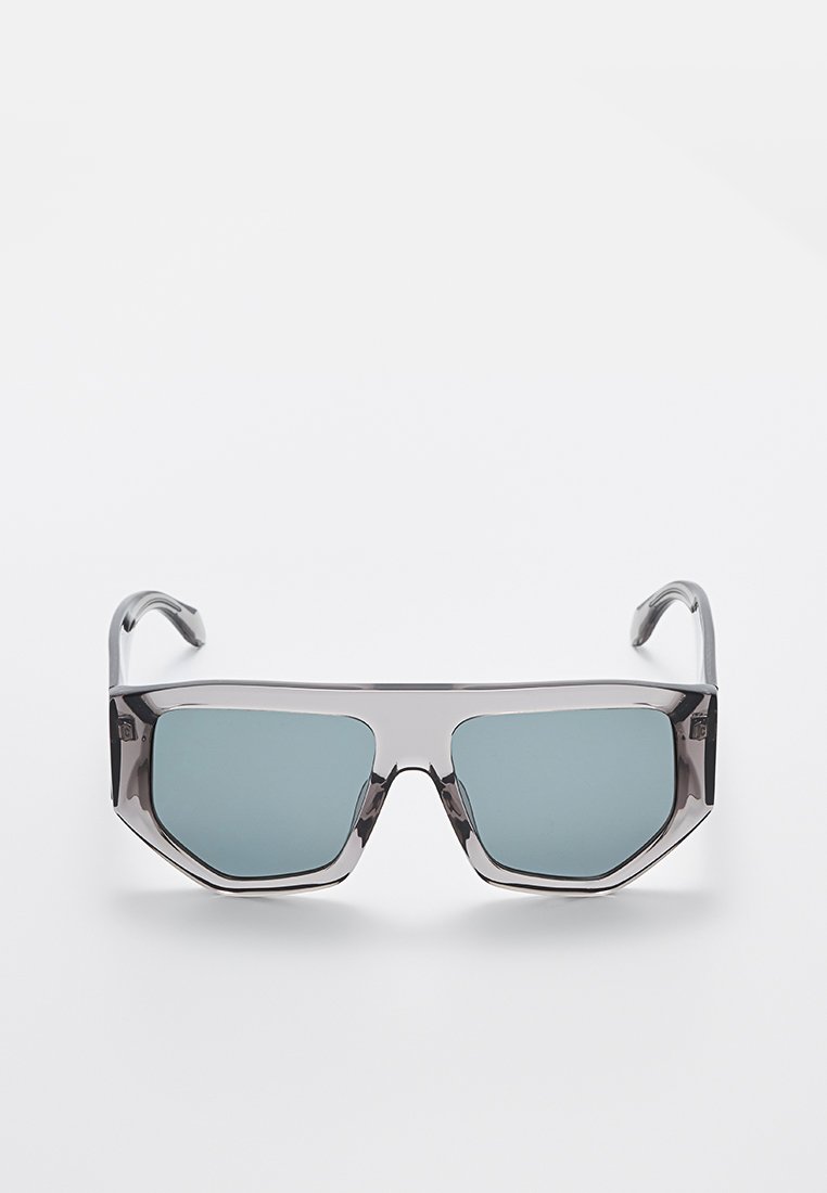 Lunettes de soleil avec une monture en plastique gris géométrique et des verres teintés bleus, présentant des bords angulaires et des branches élégantes.