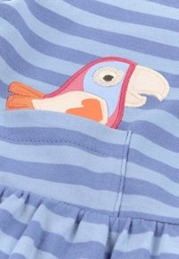 Blau gestreifter Stoff mit einem gestickten Papagei in Pink-, Orange- und Blautönen; verfügt über eine Tasche mit gerafftem Rüschendetail am Saum.