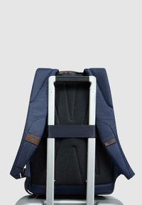 Zaino blu navy con spallacci imbottiti, pannello posteriore in rete e dettagli marroni, progettato per essere utilizzato su una valigia con ruote. Struttura solida.