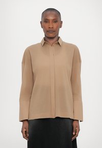 Beige button-up shirt with a collar, long sleeves, and a relaxed fit. Soft, smooth texture; no visible patterns or embellishments.