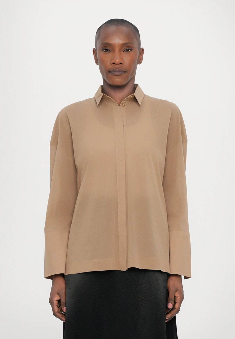 Beige button-up shirt with a collar, long sleeves, and a relaxed fit. Soft, smooth texture; no visible patterns or embellishments.