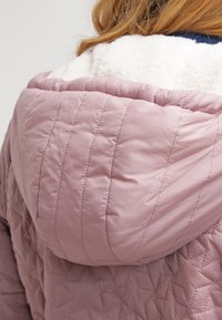 Růžová prošívaná péřová bunda s bílou kapucí podšitou fleecem, s vertikálním prošitím a měkkou texturou. Detaily zahrnují žebrovaný lem.