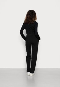 Top negro de manga larga y pantalones negros de corte relajado. Los pantalones cuentan con una cintura parcialmente elástica. Se llevan zapatillas blancas.
