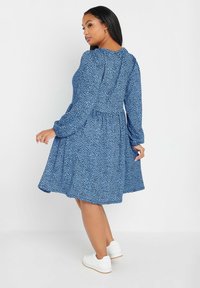 Niebieska sukienka w kwiatowy wzór z dopasowanym korpusem, rozkloszowaną spódnicą, długimi rękawami i falbaniastym dekoltem. Połączona z białymi trampkami.