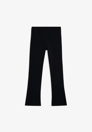 Leggings noires évasées en tissu extensible avec une texture lisse et une large ceinture ; sans logos ni motifs visibles.