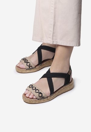 Black elastic cross straps and a woven beige upper characterize these espadrille sandals, featuring a woven jute outsole for added texture.