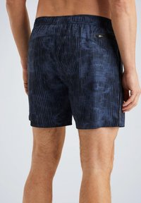 Shorts de bain bleu marine en matériau léger, présentant un motif texturé de lignes verticales, une taille élastique et une poche zippée.