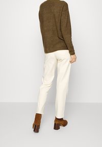 Överdimensionerad, brun stickad tröja som är parat med gräddfärgade skräddarsydda byxor. Bruna mocka anklarstövlar med klackar fulländar outfiten.