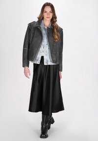 Sort læder bikerjakke med sølv hardware over en lys denimjakke, parret med en sort satin midi-nederdel og knæhøje sorte støvler.