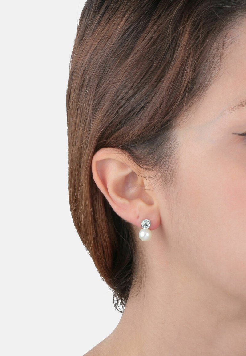 Orecchini a mo' di chiodo in argento con un cristallo trasparente rotondo sopra una perla bianca. Il design è semplice, con una finitura lucida e texture morbide.