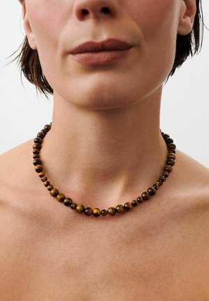 Primo piano di una persona che indossa una collana lucida con perline marroni e nere attorno al collo, con le spalle nude visibili.