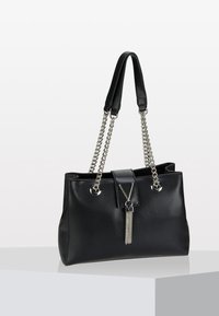Bolso de mano de cuero negro con un acabado texturizado, correas dobles de cuero y cadena, un detalle central de borlas y acentos de herrajes en tono plateado.