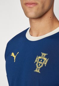 Marinblå sportströja med vit rund halsringning, med en guld Puma-logga och en guld Portugal landslagssymbol på bröstet.