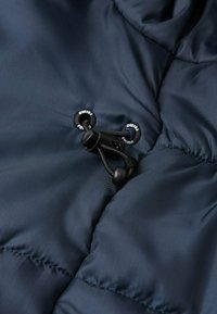 Giacca imbottita blu navy con tessuto dalla consistenza liscia, caratterizzata da hardware con cordino nero e cuciture termosaldate per una maggiore durata.