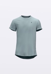 T-skjorte med korte ermer i lys blått stoff, med rund hals og en litt lengre bakre kant. Logo på brystet. Jevn tekstur.