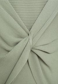 Jasnozielony materiał żebrowany skręcony w węzeł, ukazujący szczegółową teksturę i wzór rozciągnięcia.