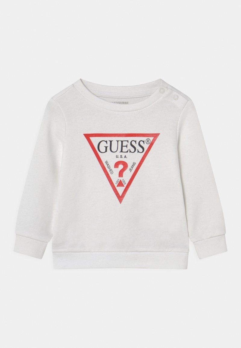 Chemise bébé blanche à manches longues avec un logo triangulaire bordé de rouge portant l'inscription "GUESS U.S.A." et deux boutons-pression sur une épaule.