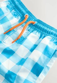 Costume da bagno a quadri blu e bianchi con elastico in vita, dotato di cordini arancioni e tessuto morbido e leggero.