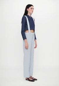 Jaqueta de denim cortada em azul escuro com fecho, detalhes de coração, combinada com calças largas em azul claro e sandálias baixas de tiras castanhas.