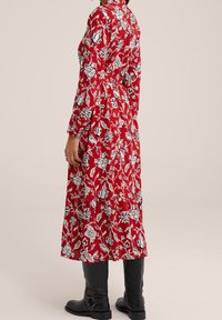 Röd blommig klänning med långa ärmar och krage, med svartvita blommönster. Matchas med svarta knähöga stövlar.