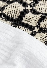 Tissu en dentelle avec des motifs floraux noirs sur un tissu blanc texturé ; présente des détails élaborés avec un schéma de couleurs contrasté.