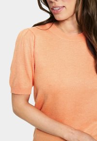 Maglione a maniche corte arancione in maglia con scollo rotondo, bordi a coste e una sottile trama. Presenta maniche a sbuffo e una silhouette aderente.