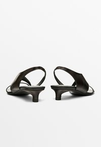 Schwarze Ledersandalen mit niedrigem, verjüngtem Absatz, offenem Rückenteil und breiten Riemen, die über den Fuß verlaufen für einen sicheren Halt. Glatte Textur, minimalistisches Design.