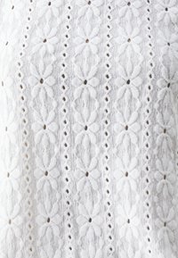 Weißer Stoff mit einem filigranen floralen Muster und strukturierten Details. Reihen von Blumen und spitzenartigen Ausschnitten erzeugen einen geschichteten Effekt.