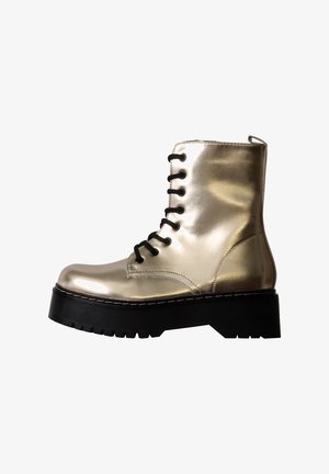 Botte de combat dorée brillante avec semelle épaisse noire à crampons et lacets noirs, vue de côté sur fond blanc.