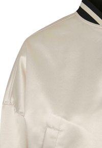 Blouson bomber en satin beige clair avec un col côtelé noir et blanc, présentant une texture lisse et un léger éclat.