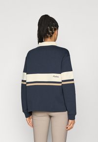 Granatowa bluza z białymi i beżowymi poziomymi paskami, z kołnierzykiem i haftowanym logo na plecach. Miękki materiał z bawełnianej mieszanki.