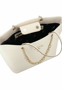 Bolso tote de cuero crema con cadena dorada y asas planas, que cuenta con un cierre magnético y un forro interior negro con un patrón de logotipos.