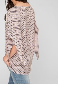 Blusa leggera e stampata con un fit morbido, maniche larghe e design off-shoulder, di un delicato beige con motivi circolari blu.