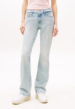 Person wearing light blue straight-leg jeans, white sneakers, and a pink sleeveless top, standing against a plain background.