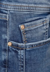 Denimjeans i en urtvård blå nyans, med kontrasterande gula stygn och en liten framficka som stängs med en kopparknapp.