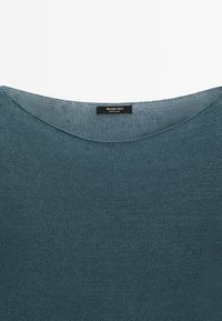 Pull en tricot bleu avec un col rond et une étiquette noire indiquant « Massimo Dutti Made in China » cousue à l'intérieur du col.