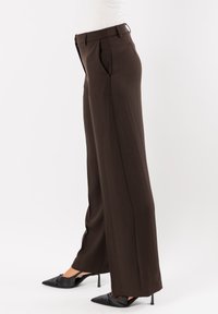 Pantaloni beige a gamba larga realizzati in tessuto morbido, con pieghe, vita aderente e tasche laterali, abbinati a tacchi a spillo neri.