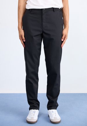Schwarze Hosen mit glatter Textur, maßgeschneiderter Passform, normalen Taschen und Knopfverschluss, kombiniert mit weißen Turnschuhen.