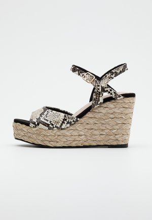 Sandalia de cuña con parte superior de estampado de serpiente en blanco y negro y plataforma de yute trenzado. Presenta una corredera para el tobillo con detalle de hebilla y diseño de punta abierta.