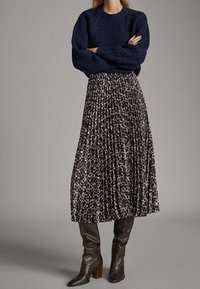 Marineblauwe gebreide trui met geribbelde textuur, gecombineerd met een geplooide midi-rok met luipaardprint. Bruine leren kniehoge laarzen met hak accentueren de look.