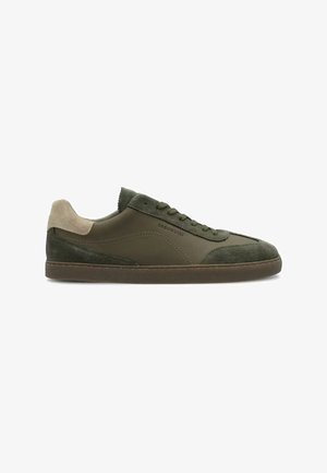 Zapatilla baja de color verde oliva con detalles de ante en la puntera y el talón, lengüeta beige en el talón, cierre con cordones y suela de goma marrón.