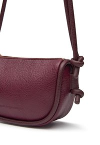 Sac en cuir bourgogne à bandoulière avec une finition texturée, une forme ronde, une fermeture éclair et des accents noués sur la sangle.
