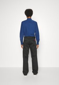 Blå långärmad skjorta med knäppta manschetter, i kombination med svarta byxor med midjeband och röd detaljer på bakfickan.