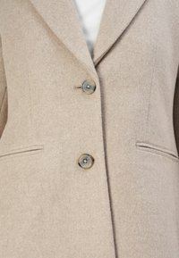 Beiger Wollmischblazer mit strukturiertem Design, zwei Knöpfen und seitlichen Taschen. Glatte Textur mit klassischem Reverskragen.