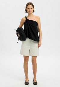 Svart topp med en axel och knutdetalj, ljusgrå shorts och en svart virkade väska. Slätt tyg, lös passform och svarta platta skor.
