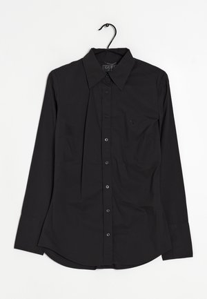 Sort langærmet skjorte med knapper og spids krave på en bøjle, med en lille broderet logo på venstre bryst.