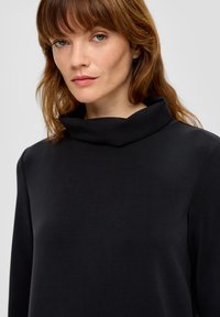 Czarny top z wysokim kołnierzem, z długimi rękawami, gładka tkanina, luźny krój, z zagiętym kołnierzem i minimalistycznym designem.