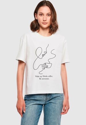 T-shirt en coton blanc avec un dessin simple en ligne noire d'un visage tenant une tasse de café et le texte : "Réveille-toi. Bois du café. Sois génial."