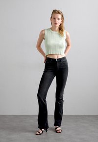 Light green ribbed crop top, black flared jeans, and black strappy heels. Simple design with textured patterns and fitted silhouette.